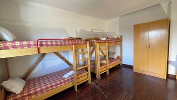 Habitación con literas, suelo de madera, un armario y una lámpara en el techo.