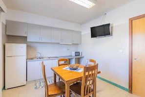 Uma cozinha compacta com geladeira, micro-ondas e TV fixada na parede.