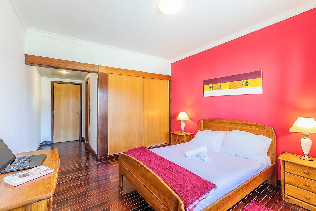 Une chambre d’hôtel avec un lit, des meubles en bois, un bureau avec un ordinateur portable et un mur rouge.