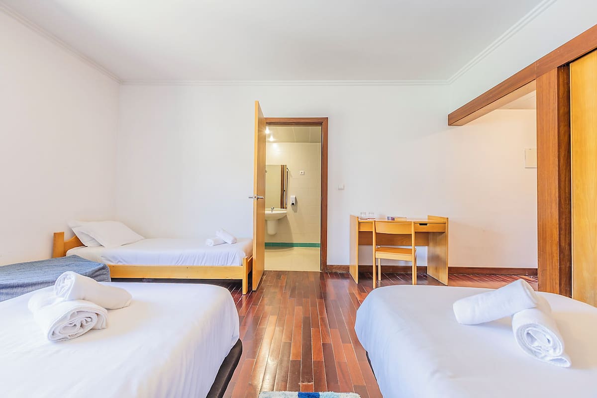 Une chambre d’hôtel avec deux lits, un bureau et une salle de bain visible à travers une porte ouverte.
