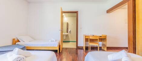 Habitación de hotel con dos camas, un escritorio y un baño visible a través de una puerta abierta.
