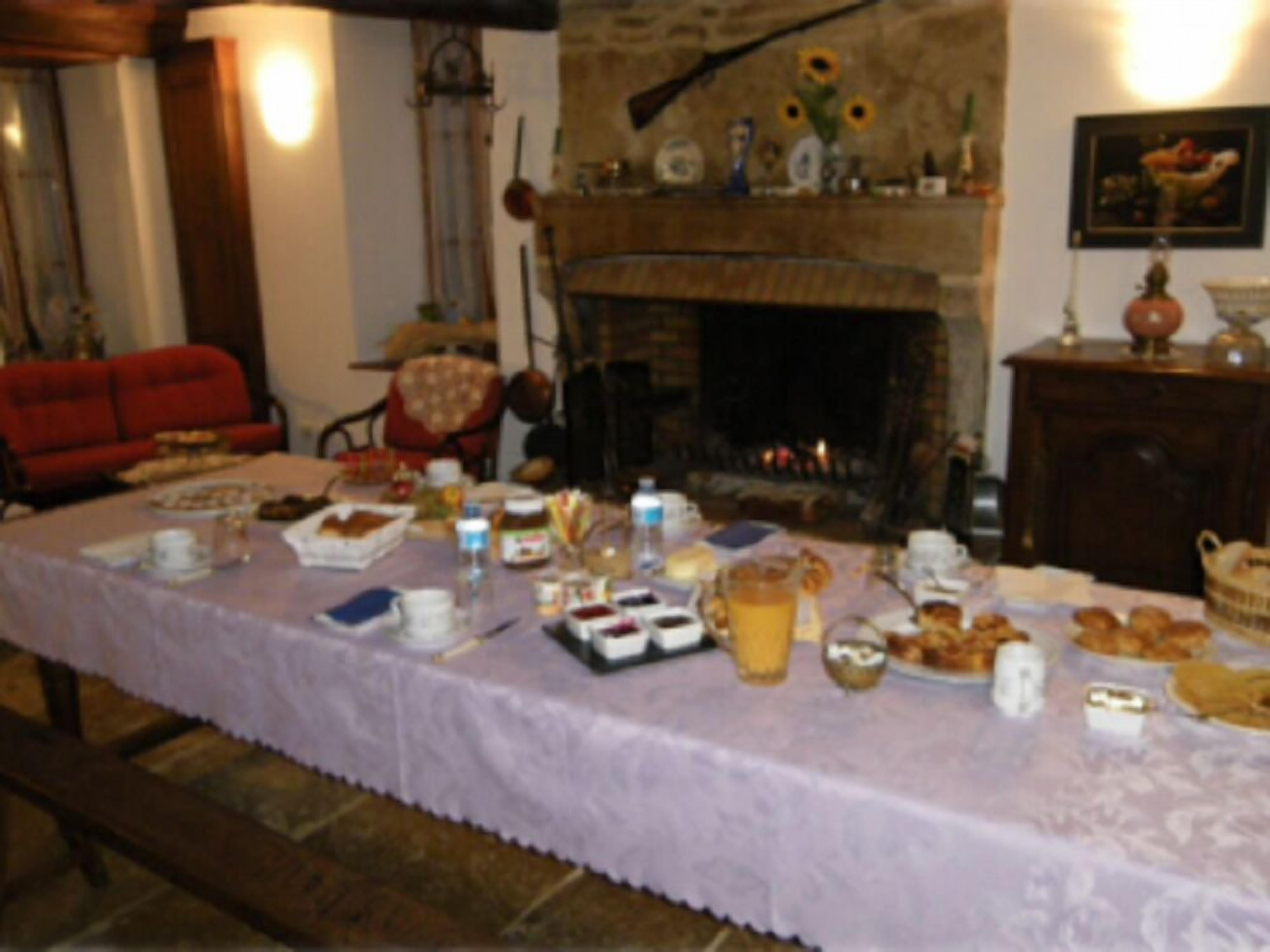 Un comedor con una larga mesa dispuesta para el desayuno, una chimenea y un sofá rojo.