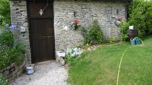 A stone building with a dark wooden door, a gravel path, and flower boxes on the wall. - La Ferme du Coucou (Prenois)