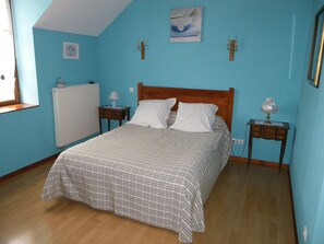 A bedroom with a bed, a nightstand, a lamp, a picture on the wall, and a window.