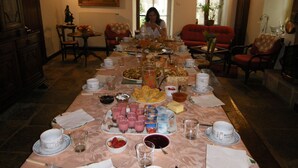 A dining table set with various dishes, glasses, and utensils, surrounded by chairs and a sofa in a room with a large window and a painting on the wall. - La Ferme du Coucou (Prenois)