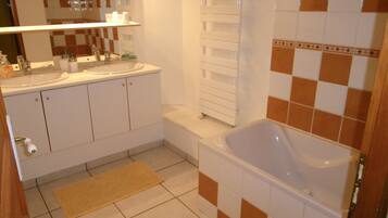 A bathroom with a bathtub, two sinks, a mirror, and a towel rack.