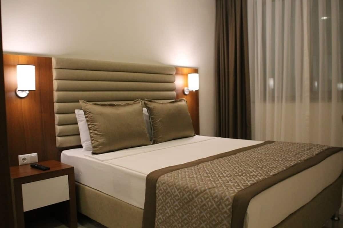 Una habitación de hotel con cama, mesitas de noche, lámparas y una ventana con cortinas.