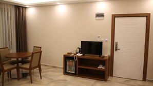 A hotel room with a dining table and chairs, a television, a mini-fridge, and a door. - Erzincan Mesut Hotel (Erzincan)