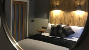A bedroom with a bed, a wooden headboard, two bedside lamps, a nightstand, and a door with vertical stripes. - Rosemount Boutique B&B (Lanark)