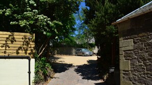 A narrow driveway leading to a parked car, flanked by a wooden fence and a stone wall. - Rosemount Boutique B&B (Lanark)
