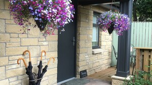 A stone building with hanging flower baskets and two umbrellas leaning against the wall. - Rosemount Boutique B&B (Lanark)