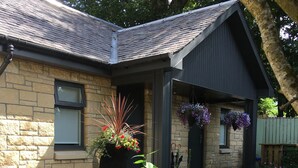 A stone building with a dark roof, a black door, and a hanging flower basket. - Rosemount Boutique B&B (Lanark)