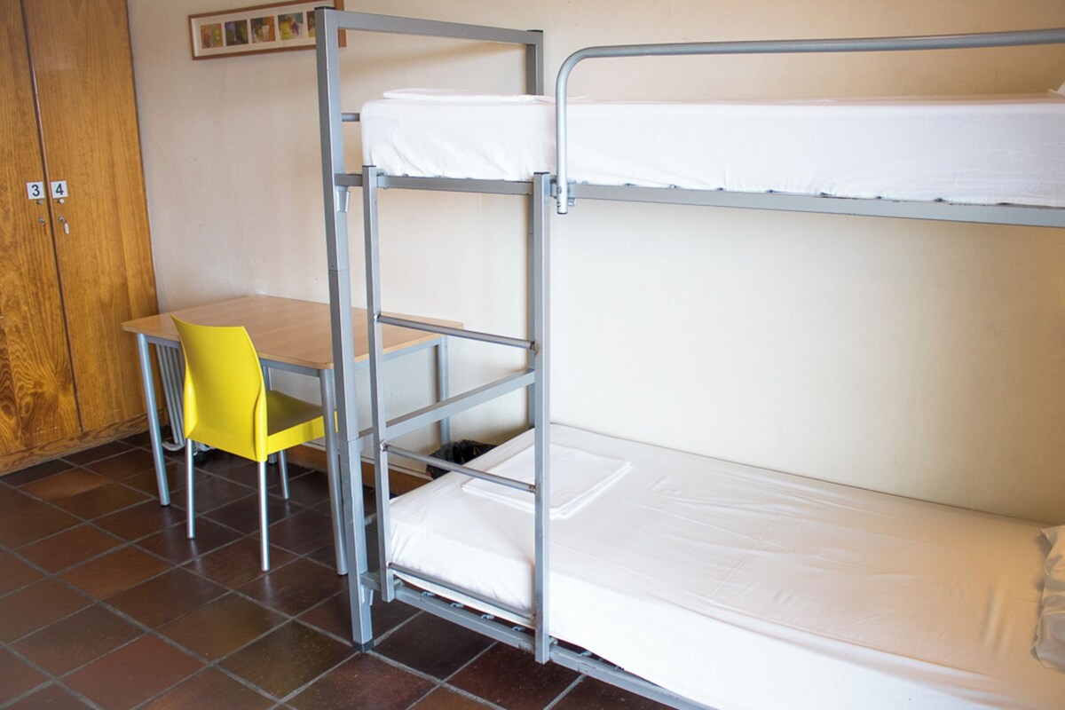 Una cama litera con escritorio y silla, una puerta de madera y un suelo de baldosas.