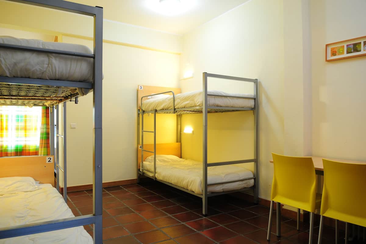 Ein Schlafsaalzimmer mit Etagenbetten, einem Schreibtisch und zwei Stühlen.