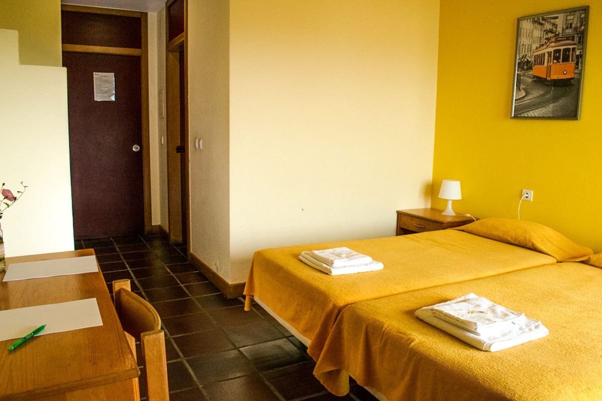 Ein Hotelzimmer mit zwei Betten, einem Schreibtisch mit Stuhl, einem Nachttisch mit Lampe und einem Bild an der Wand.