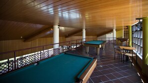 A pool table and a billiards table in a room with wooden ceilings and tiled flooring.