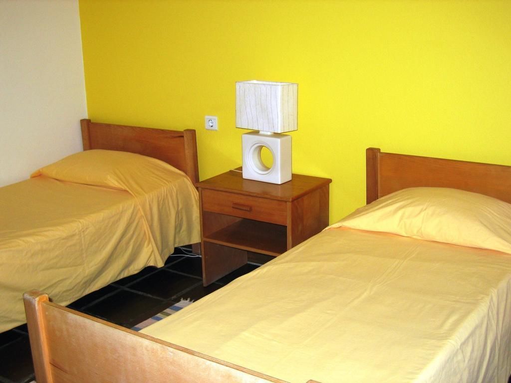 A room with two beds, a nightstand with a lamp, and a yellow wall.