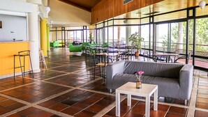 A spacious indoor area with a wooden ceiling, large windows, and a mix of seating arrangements including a sofa and tables.