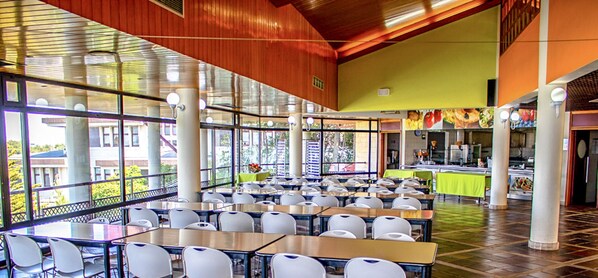 A cafeteria with tables and chairs, large windows, and a counter with food displays. - HI Almada - Pousada Juventude - Hostel (Almada)