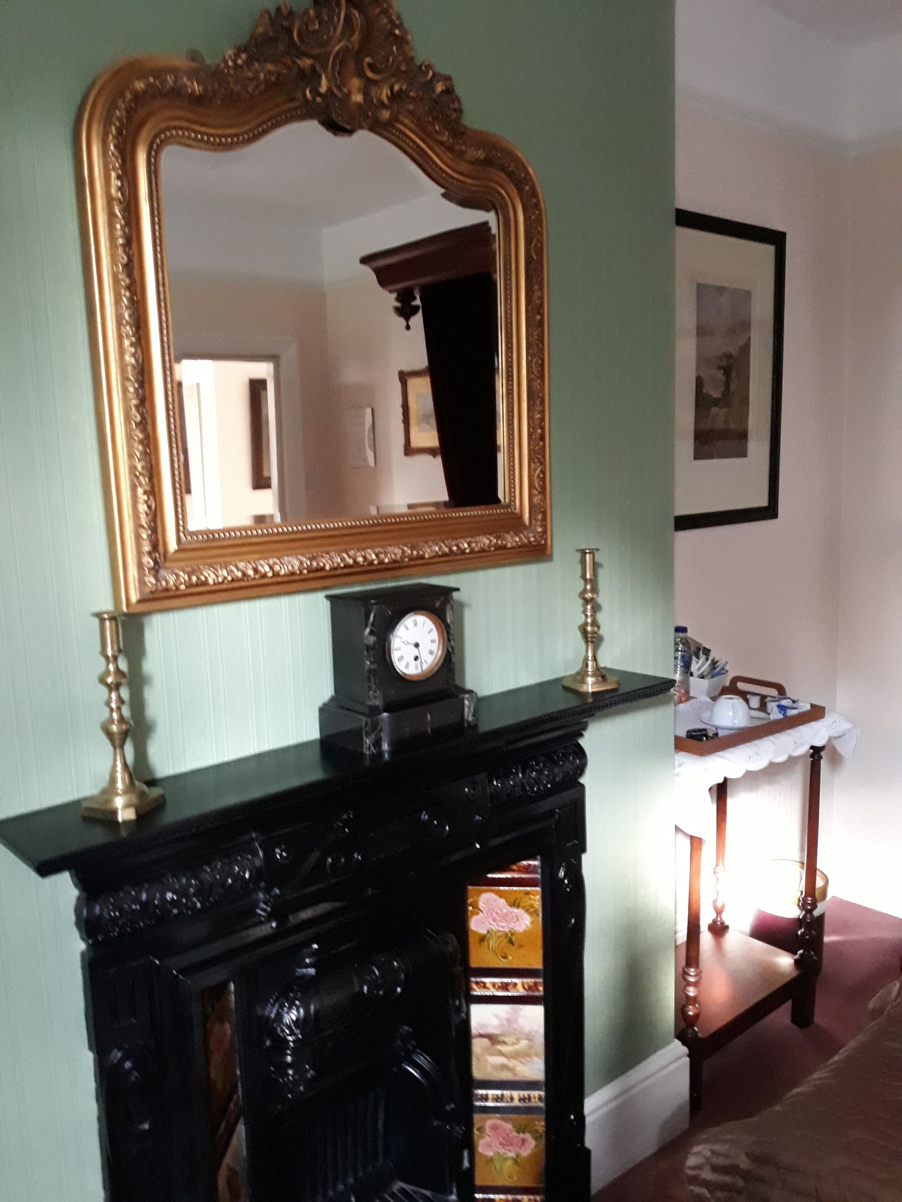 A room with a black fireplace, a gold-framed mirror, and a clock above it.