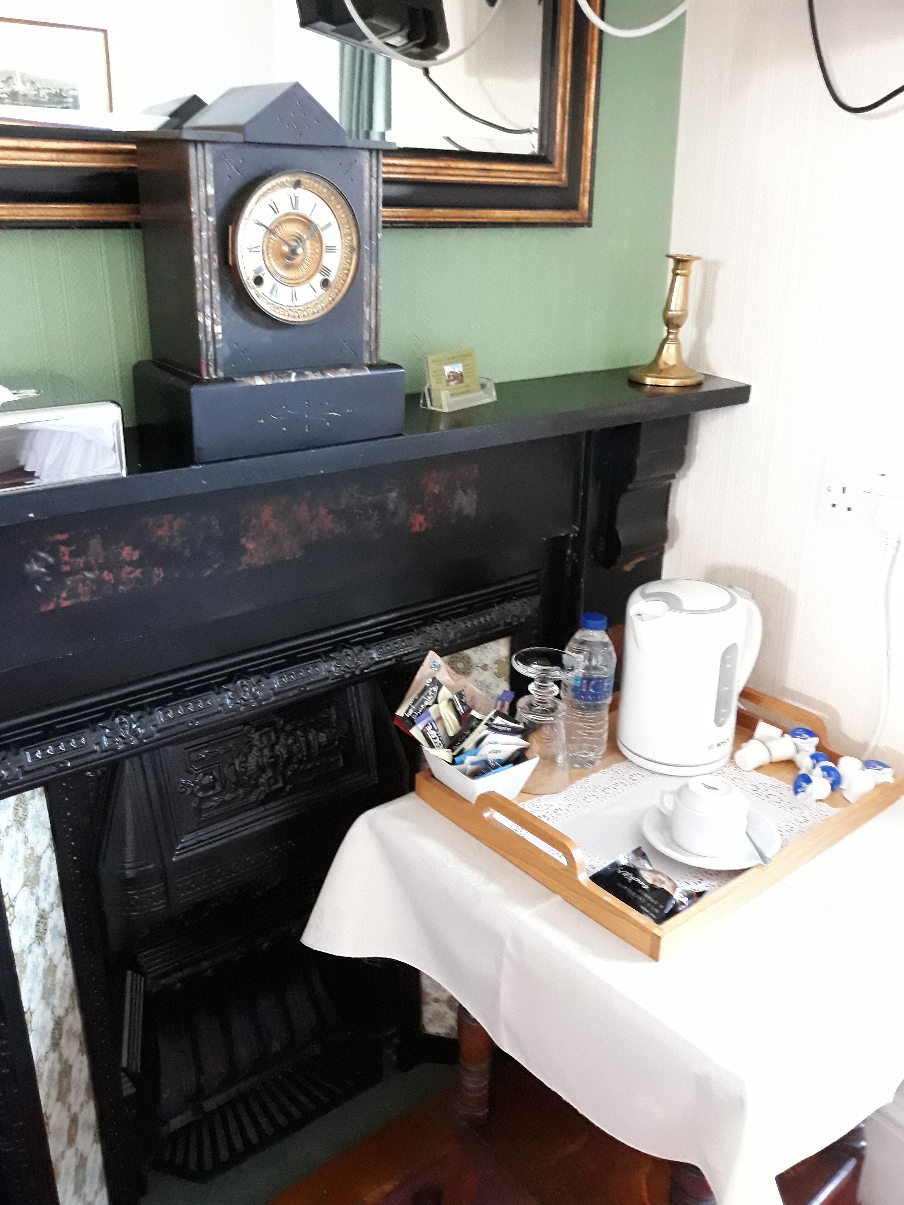 Una habitación con chimenea, un reloj, una bandeja con una cafetera y una botella de agua.
