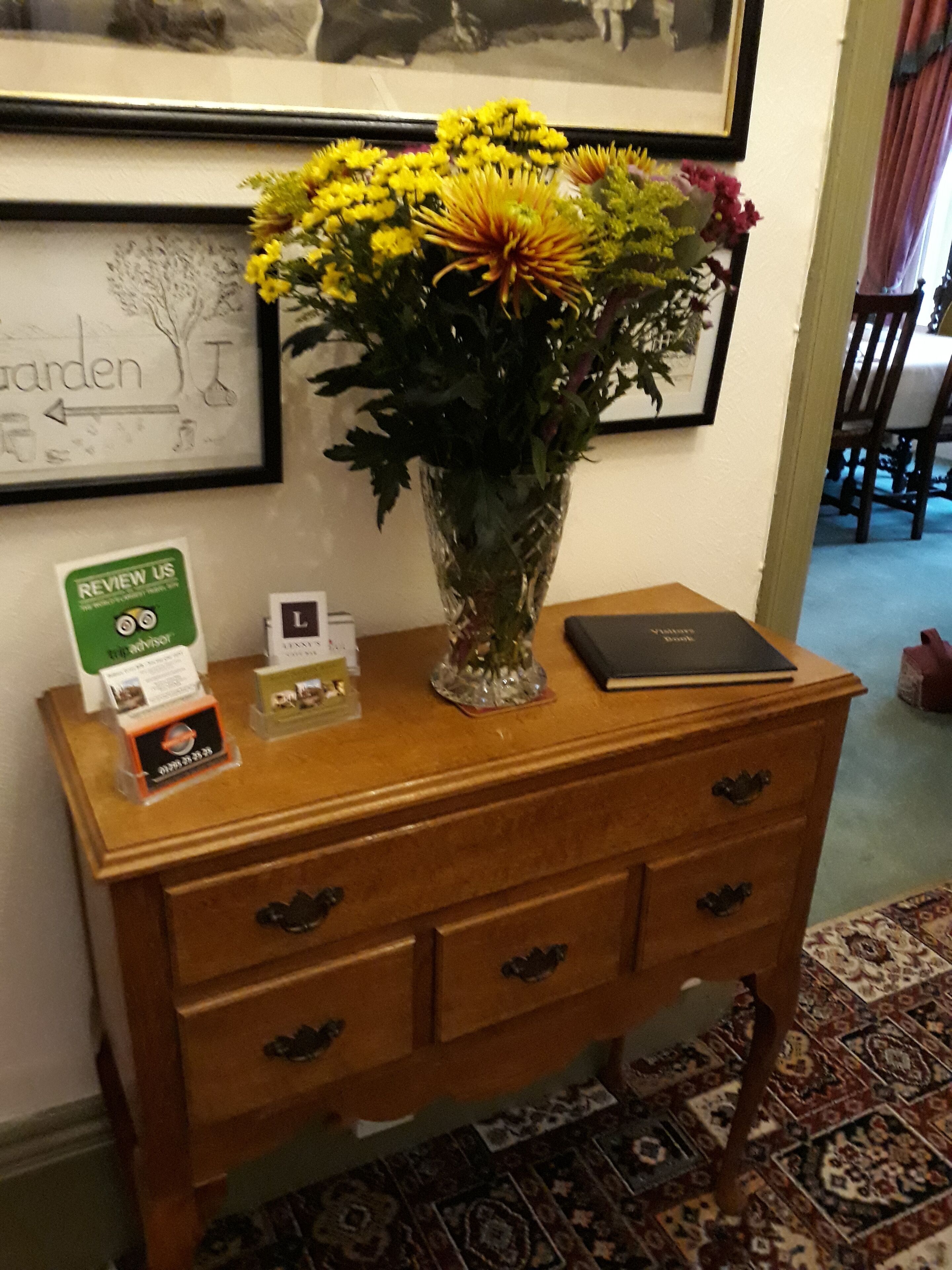 Een houten bijzettafeltje met een vaas met gele bloemen, een ingelijst foto en een klein bordje.