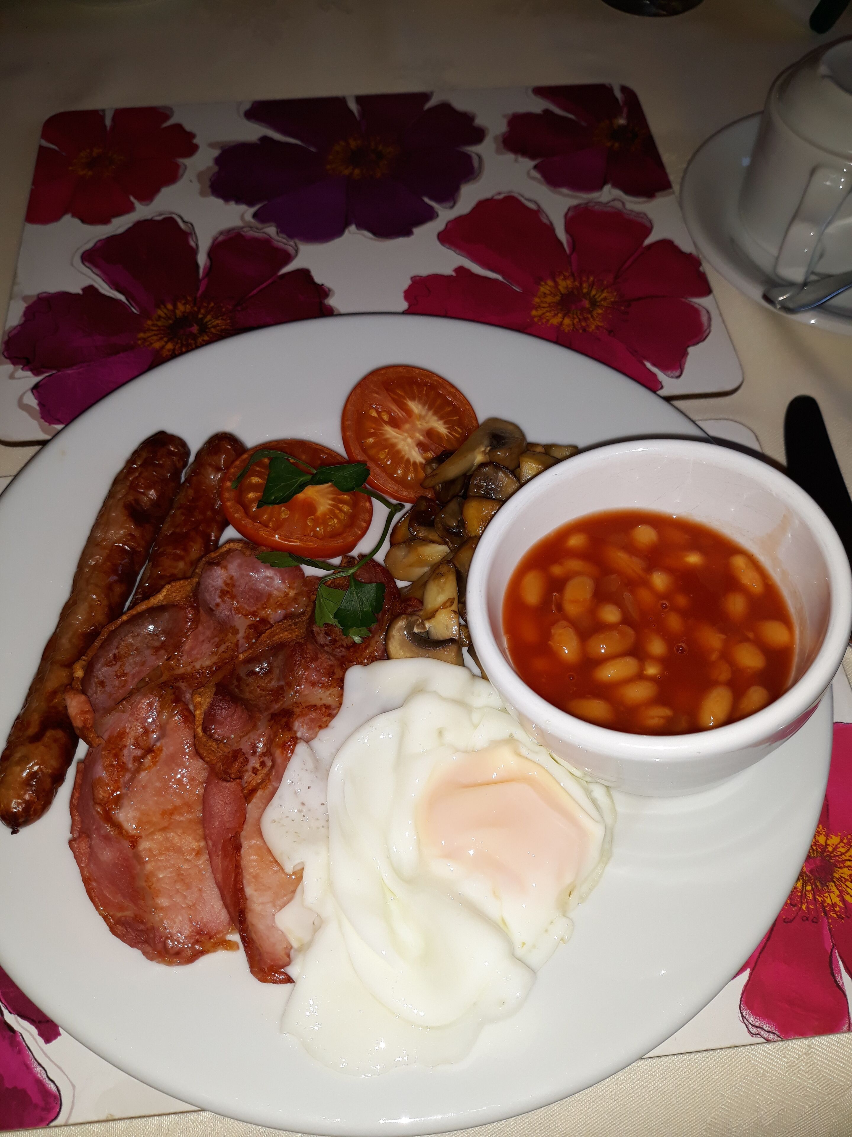 Un plato de comida para el desayuno con salchichas, tocino, huevos, tomates, champiñones y frijoles.