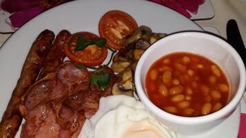 Un plato de comida para el desayuno con salchichas, tocino, huevos, tomates, champiñones y frijoles.