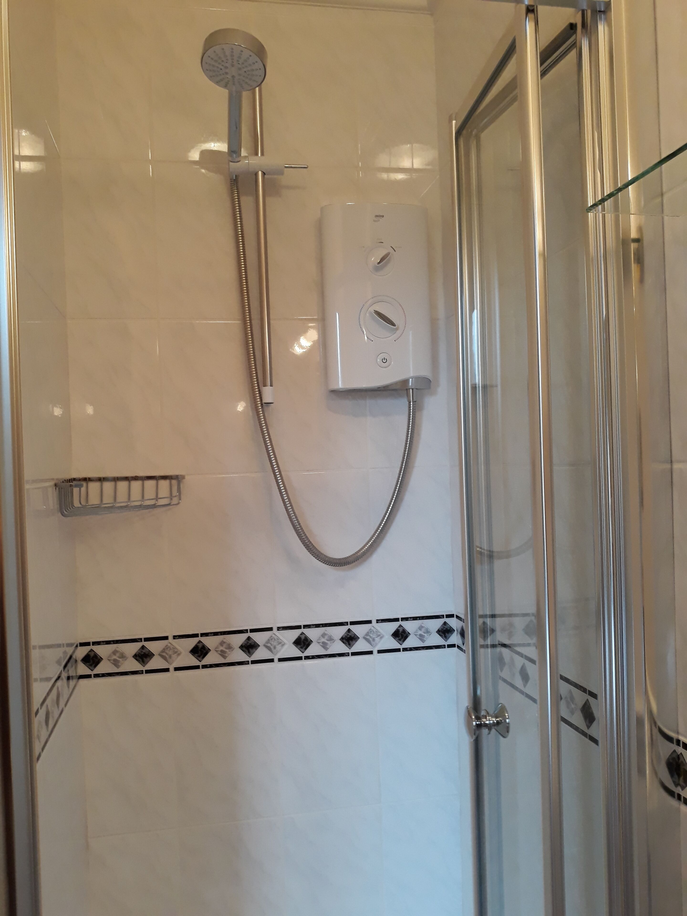 A shower with a handheld showerhead, a control panel, and a glass door.