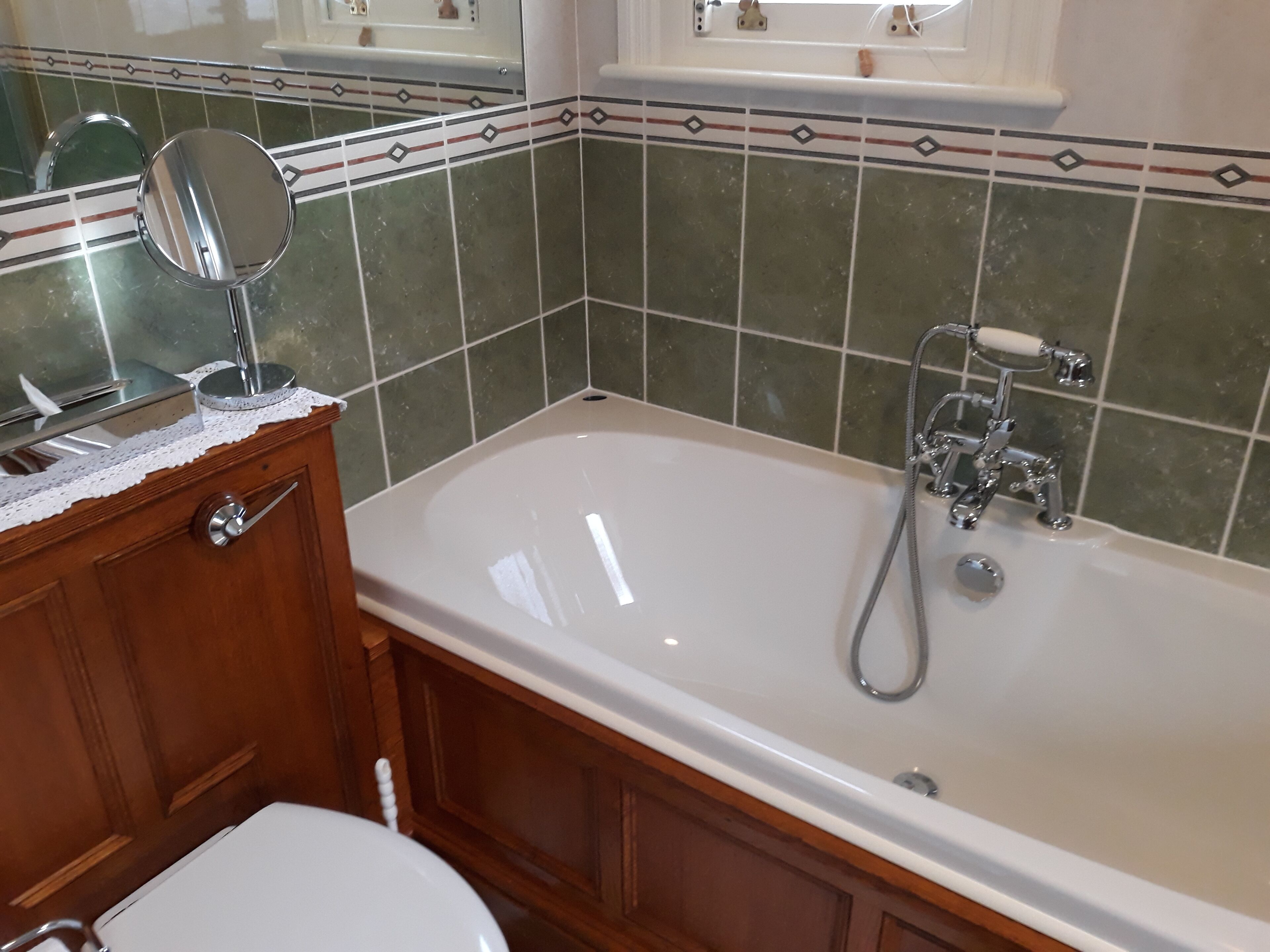 A bathroom with a bathtub, a wooden vanity, a mirror, and a toilet.