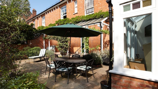 Une terrasse avec une table et des chaises, un parasol vert et un bâtiment en briques en arrière-plan.