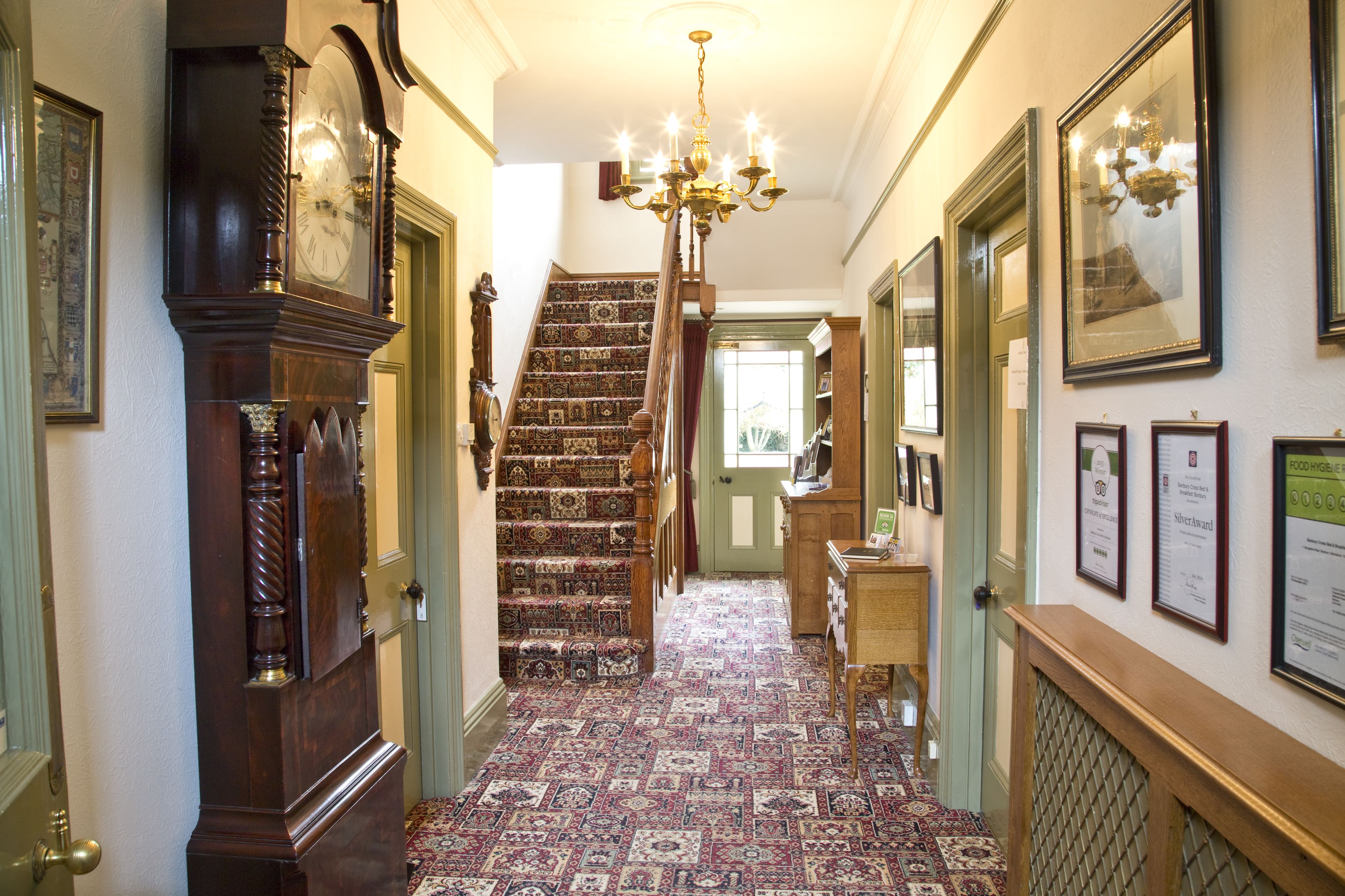 A hallway with a patterned carpet, a grand staircase, and a chandelier.