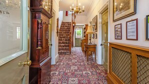Un vaste hall d’entrée avec un tapis à motifs, un escalier en bois et un lustre.