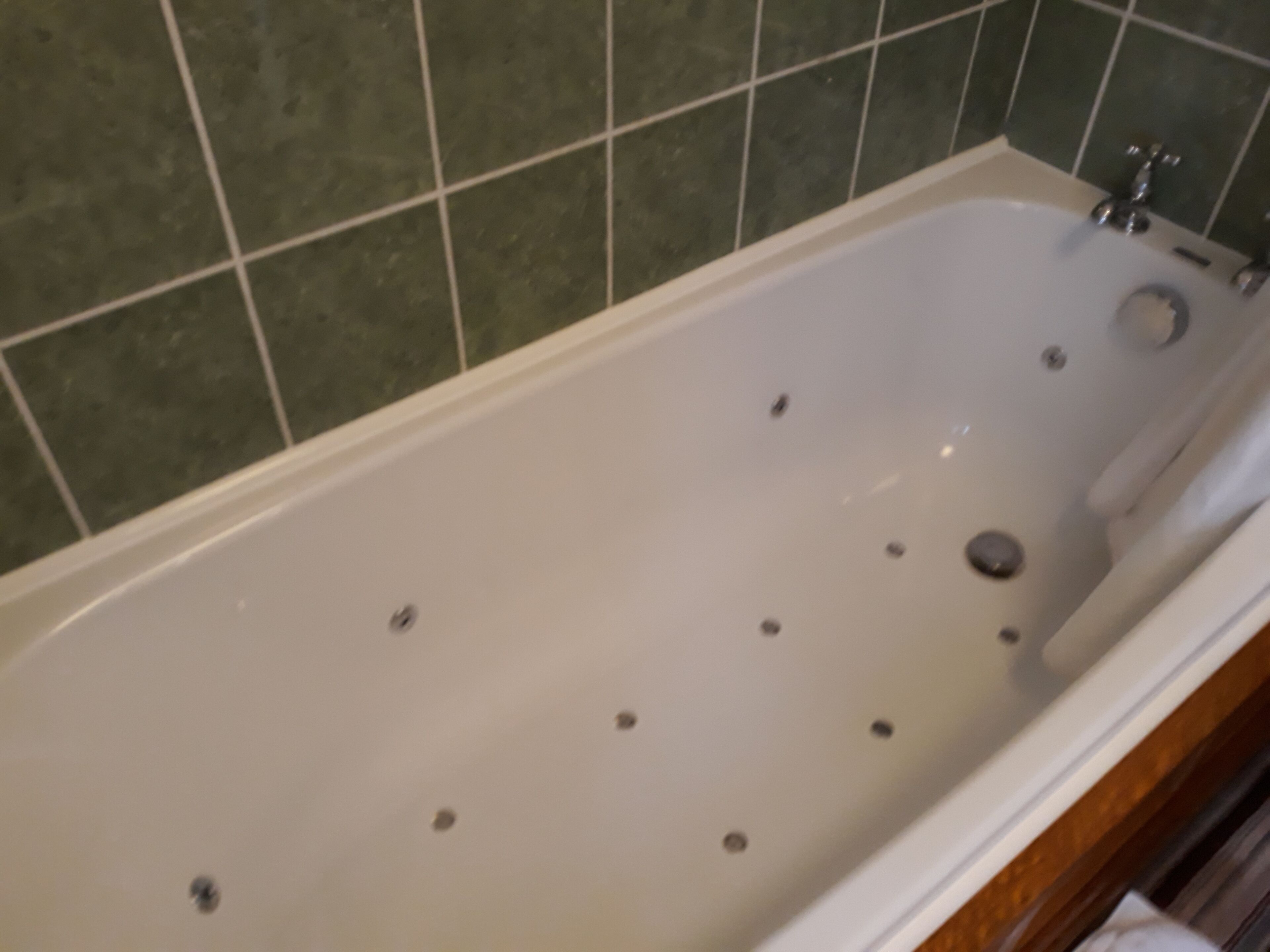 A bathtub with multiple faucets and a single drain, set against a tiled wall.