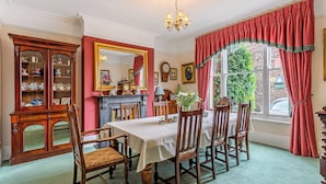 Une salle à manger avec une table dressée pour six personnes, entourée de chaises en bois. Un buffet en bois, doté de portes en verre, se trouve à gauche, et un grand miroir est accroché au-dessus de la table.
