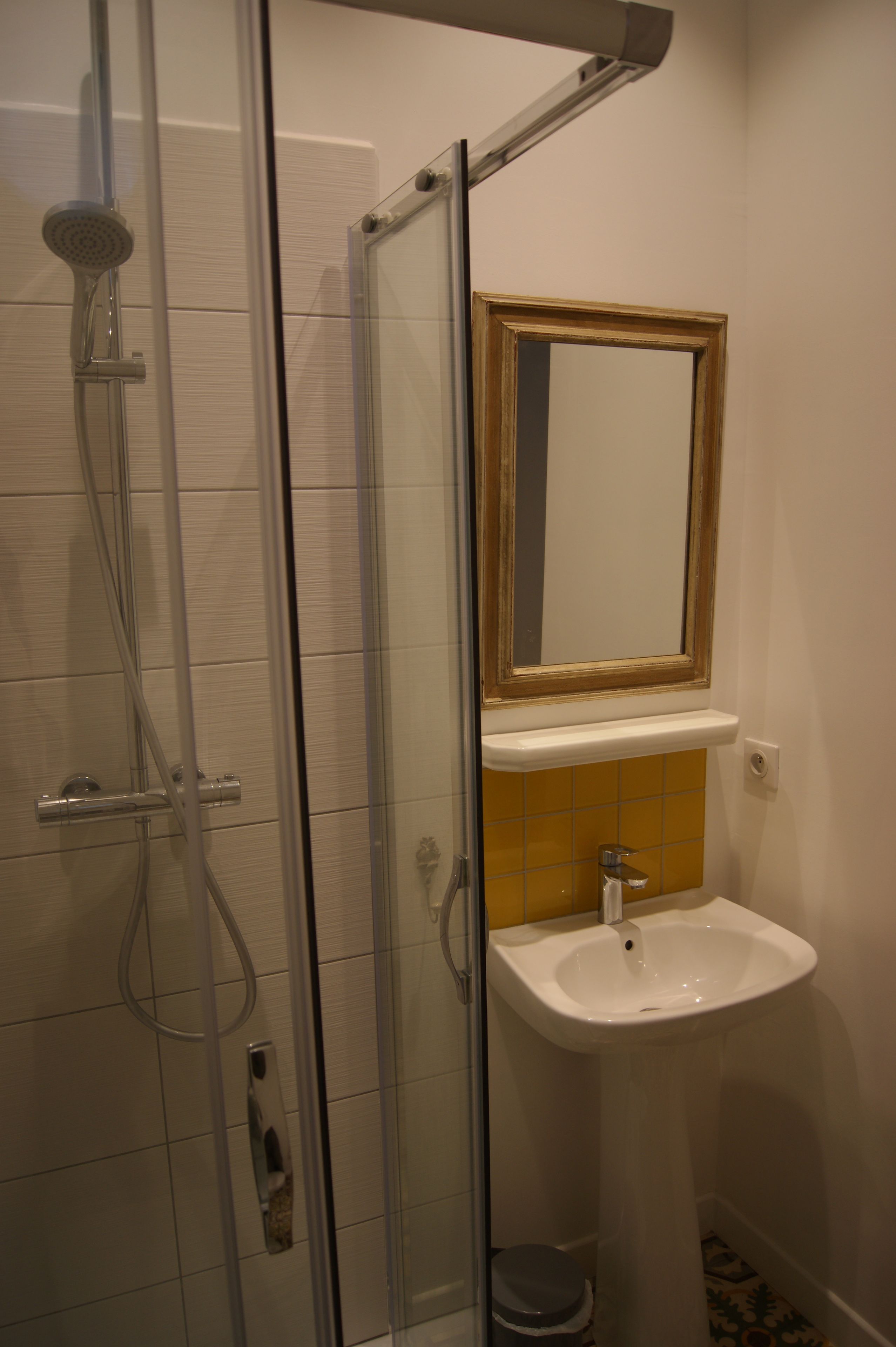 A bathroom with a glass shower enclosure, a white sink, and a mirror above it.