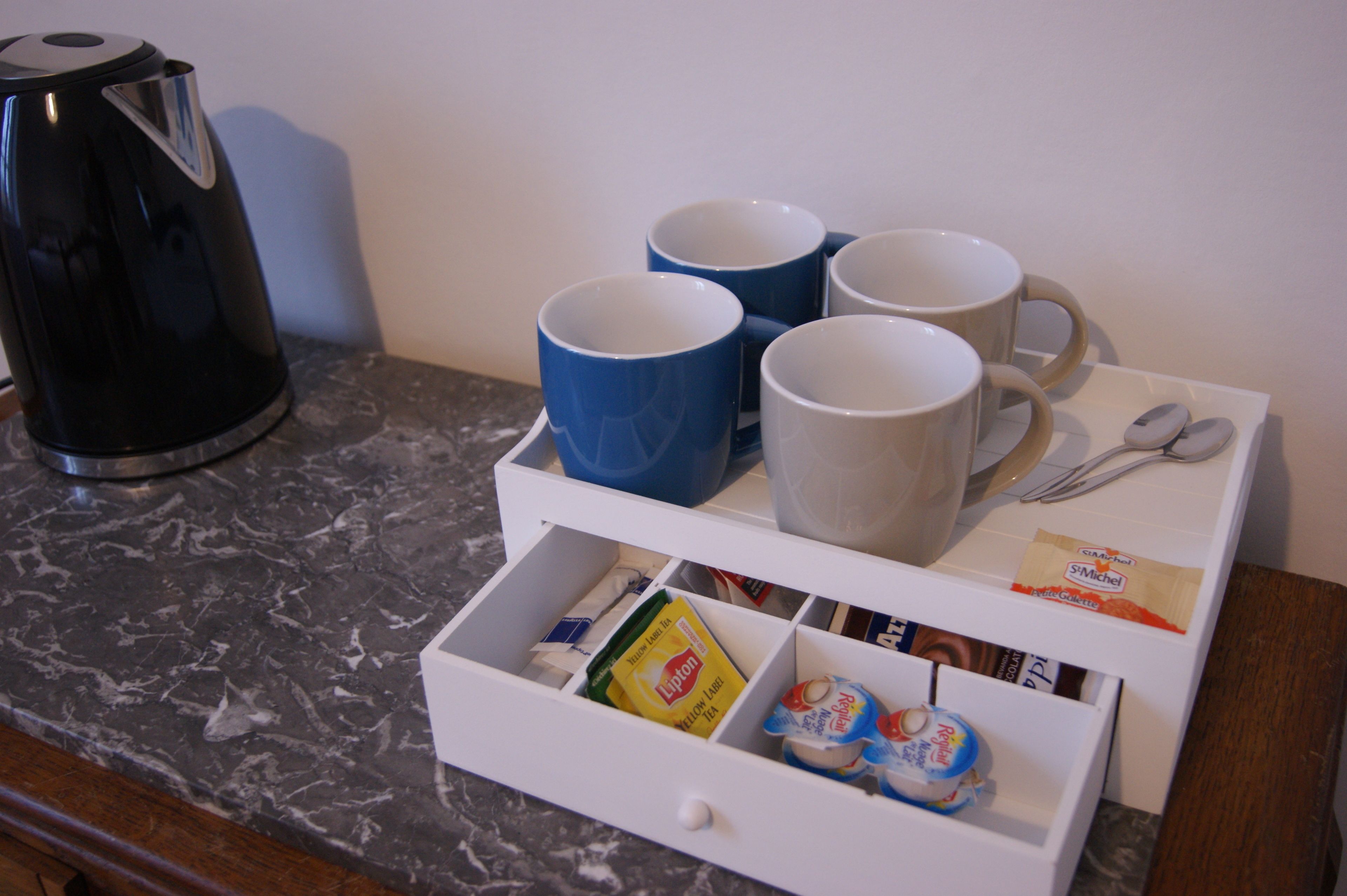 Eine Küchenarbeitsplatte mit Kaffeemaschine, einer Schublade für Küchenutensilien und einem Tablett mit Tassen und Besteck.