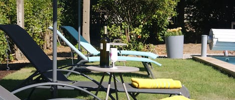 Een zwembadgedeelte met ligbedden, een tafel met een fles en een afvalbak.