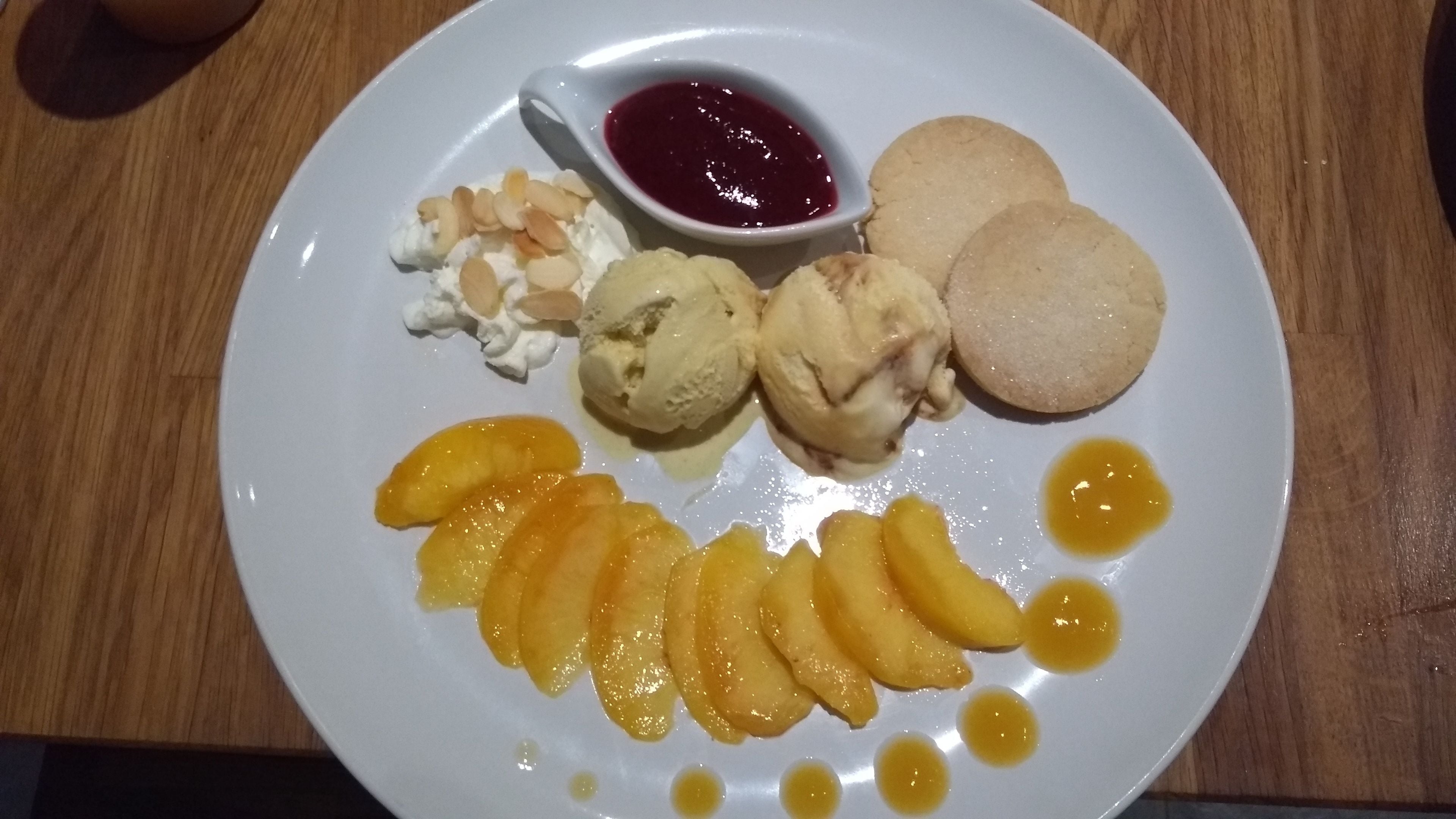 Une assiette avec de la glace, des biscuits et des tranches de pêche.