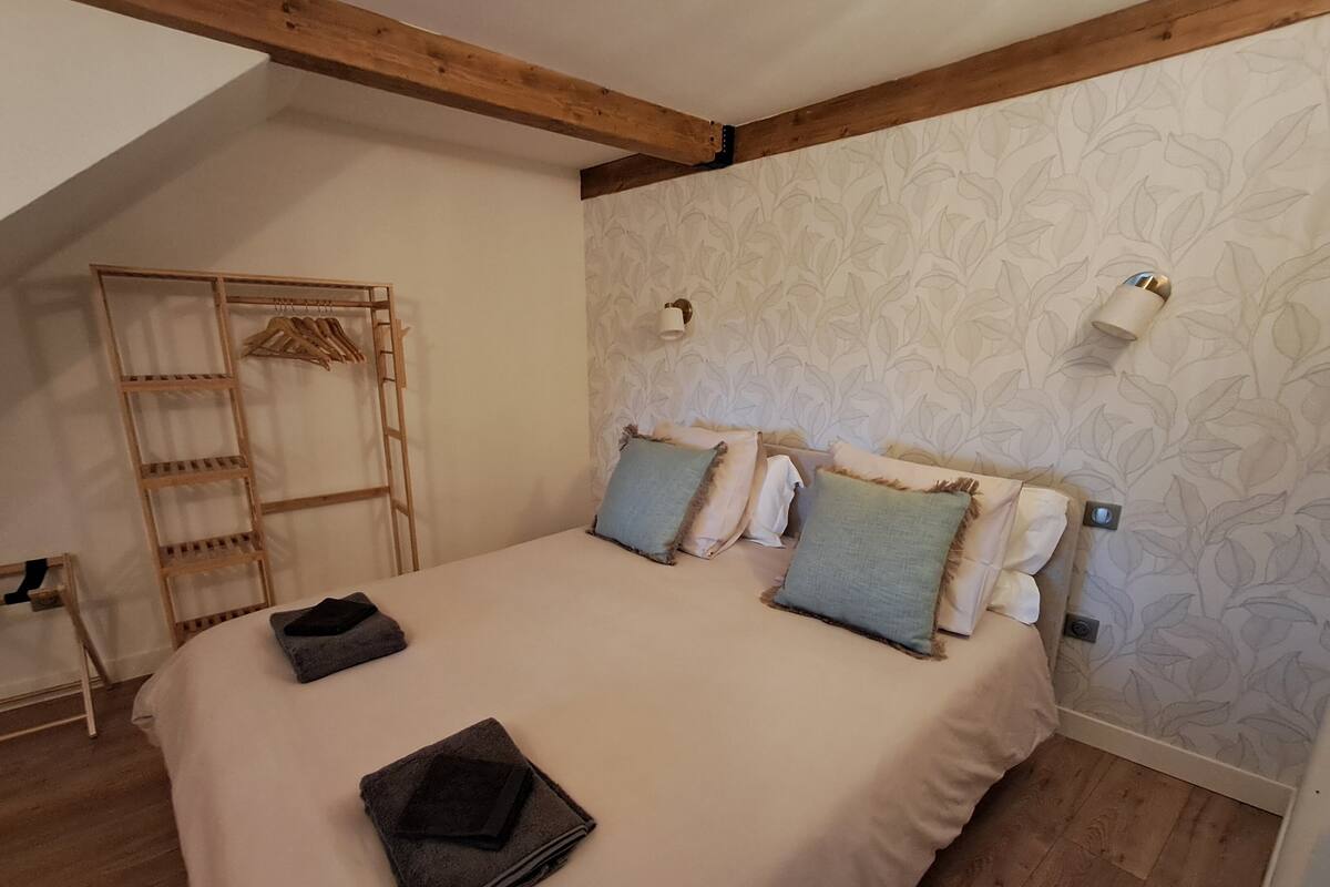 Ein Schlafzimmer mit Holzboden, einem Bett mit beiger Bettdecke, zwei Kissen, einer Holzleiter und einer Wand mit Blattmuster.