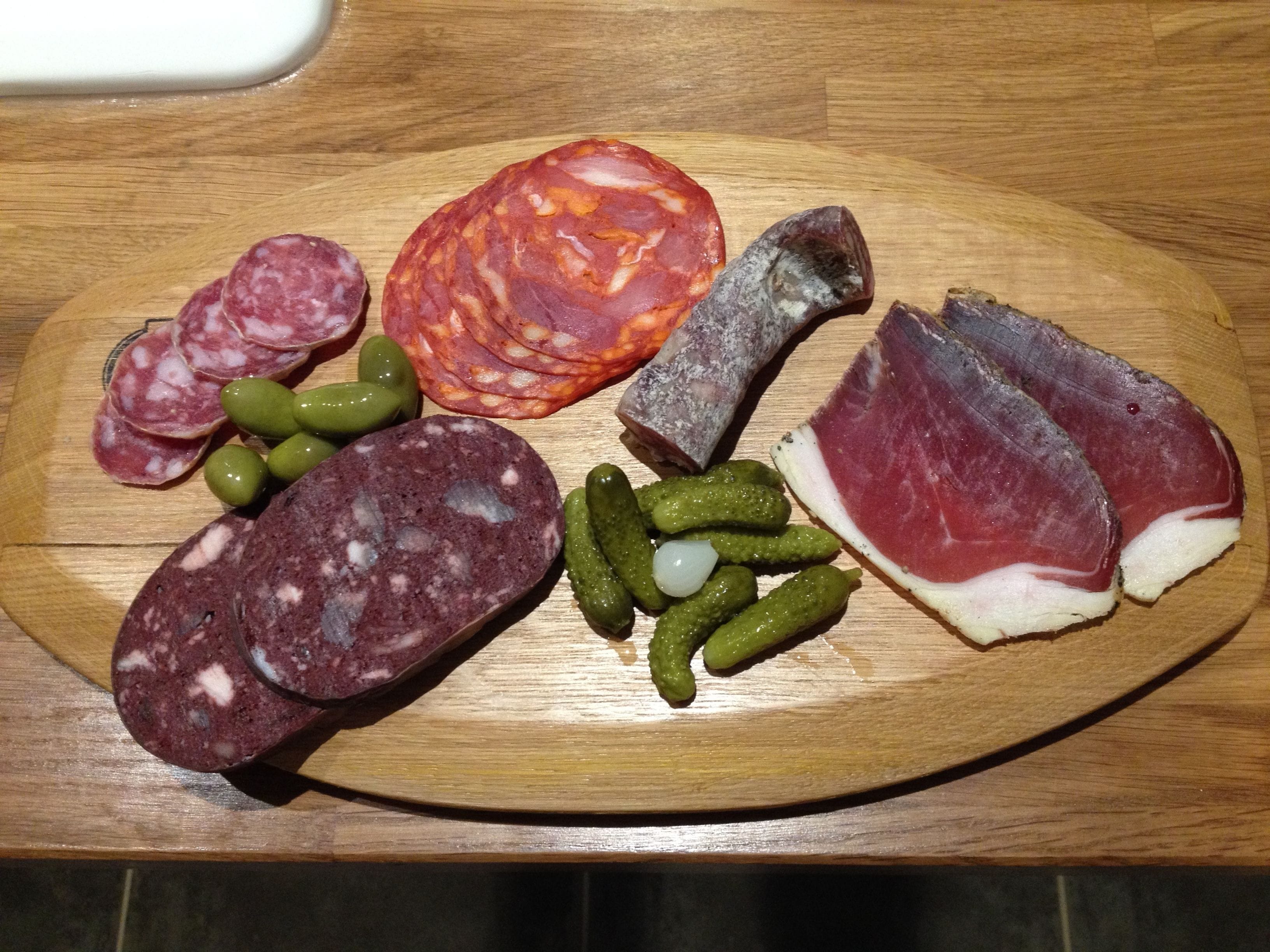 A wooden board with various cured meats and olives.