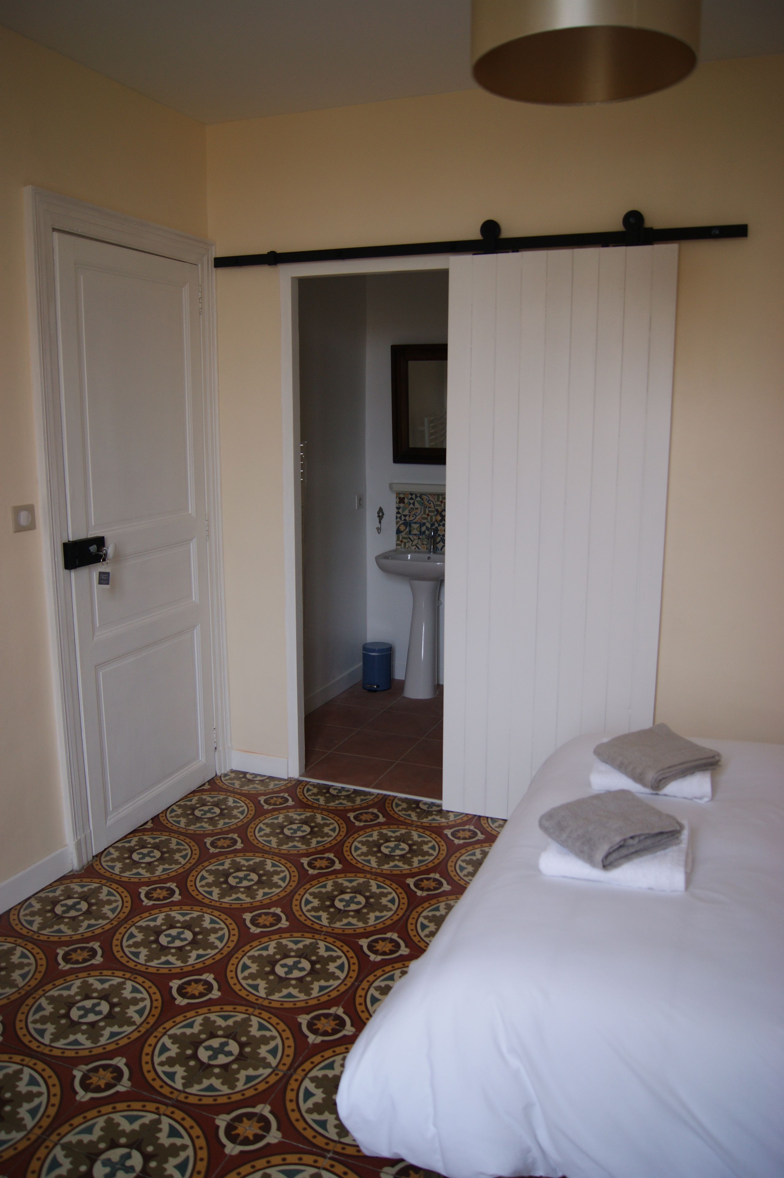 Hotelkamer met een patroon vloer, een bed met witte lakens en twee kussens, een witte deur, en een zichtbare badkamer door een open deur.