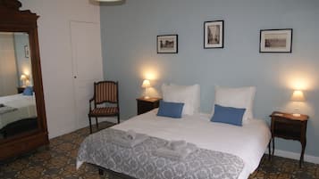 Habitación de hotel con una cama grande, dos mesitas de noche con lámparas, una silla, un espejo y tres cuadros en la pared.