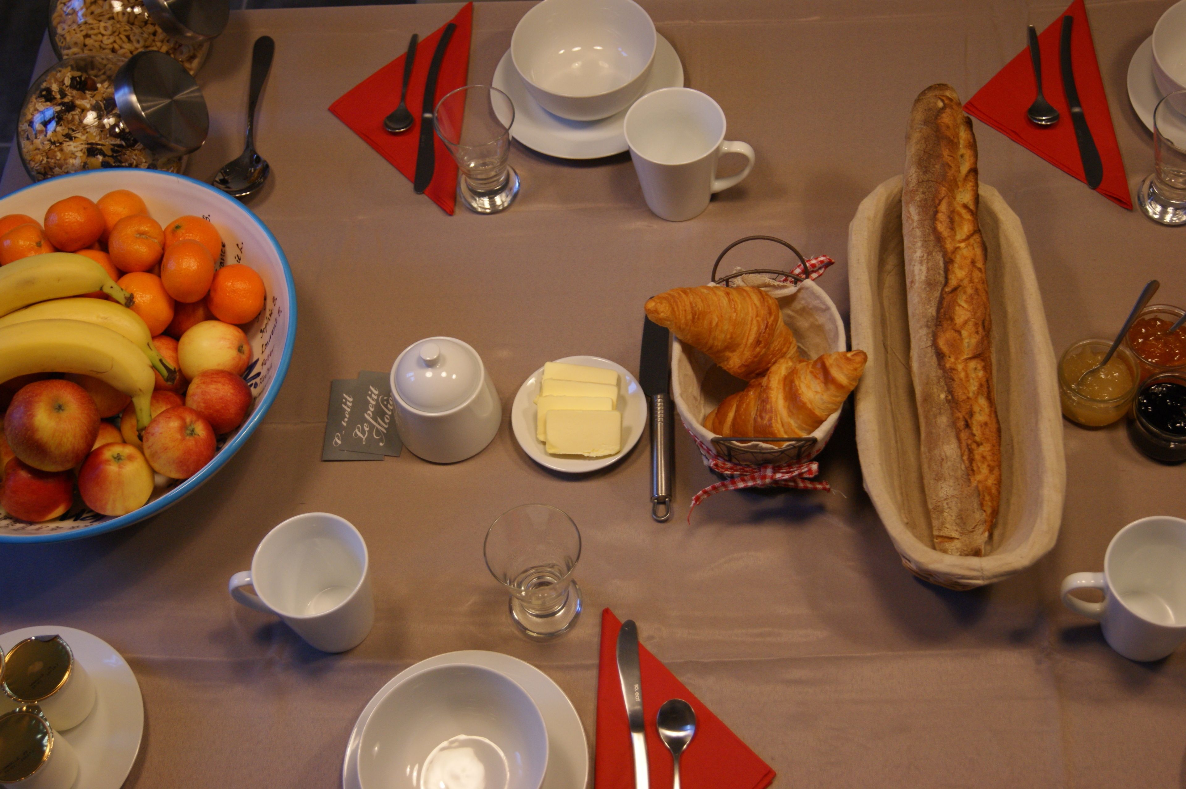 Ein Frühstückstisch mit Früchten, Brot, Butter und Besteck.