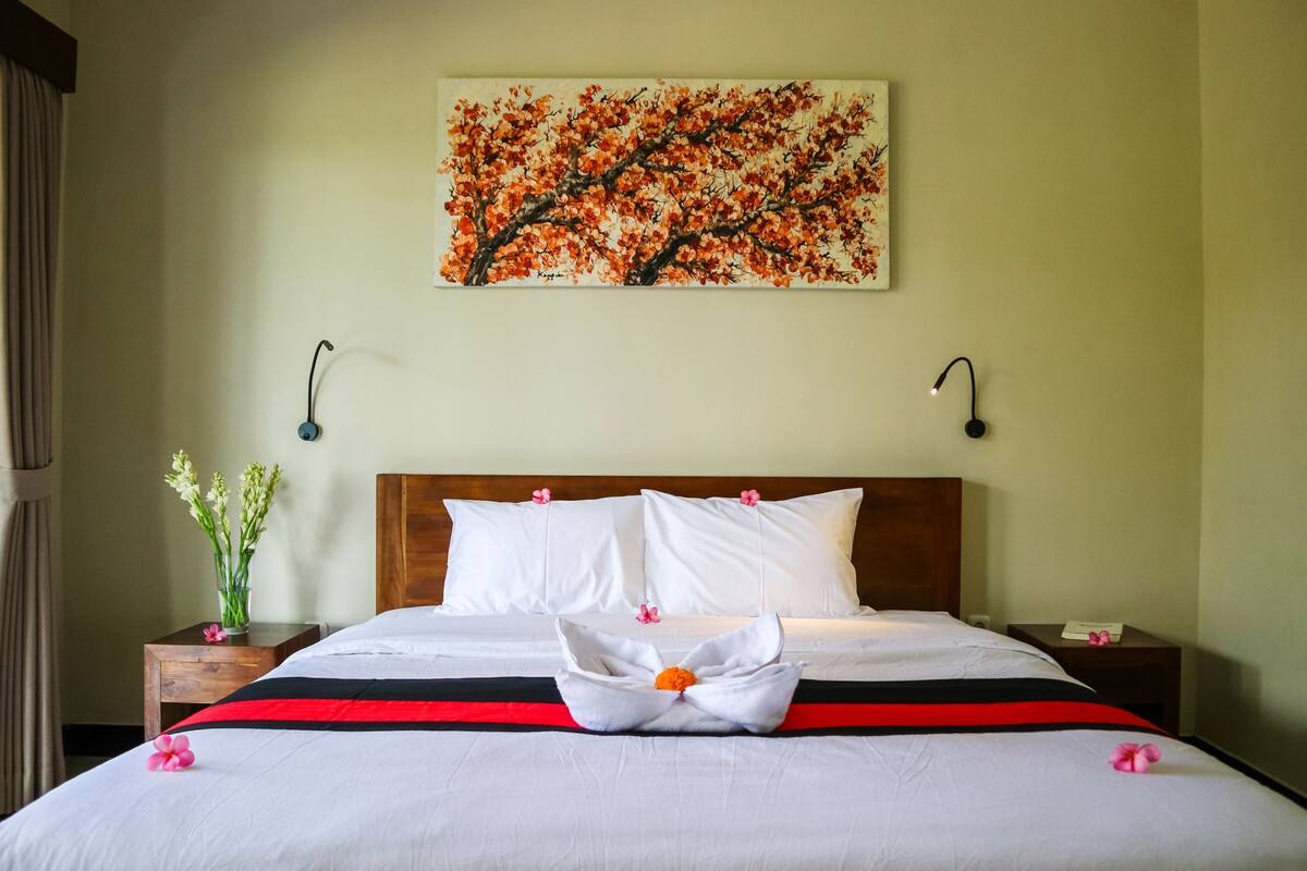 Un letto rifatto con lenzuola bianche, una coperta a letto bicolor rossa e nera e un'elegante composizione floreale al centro.