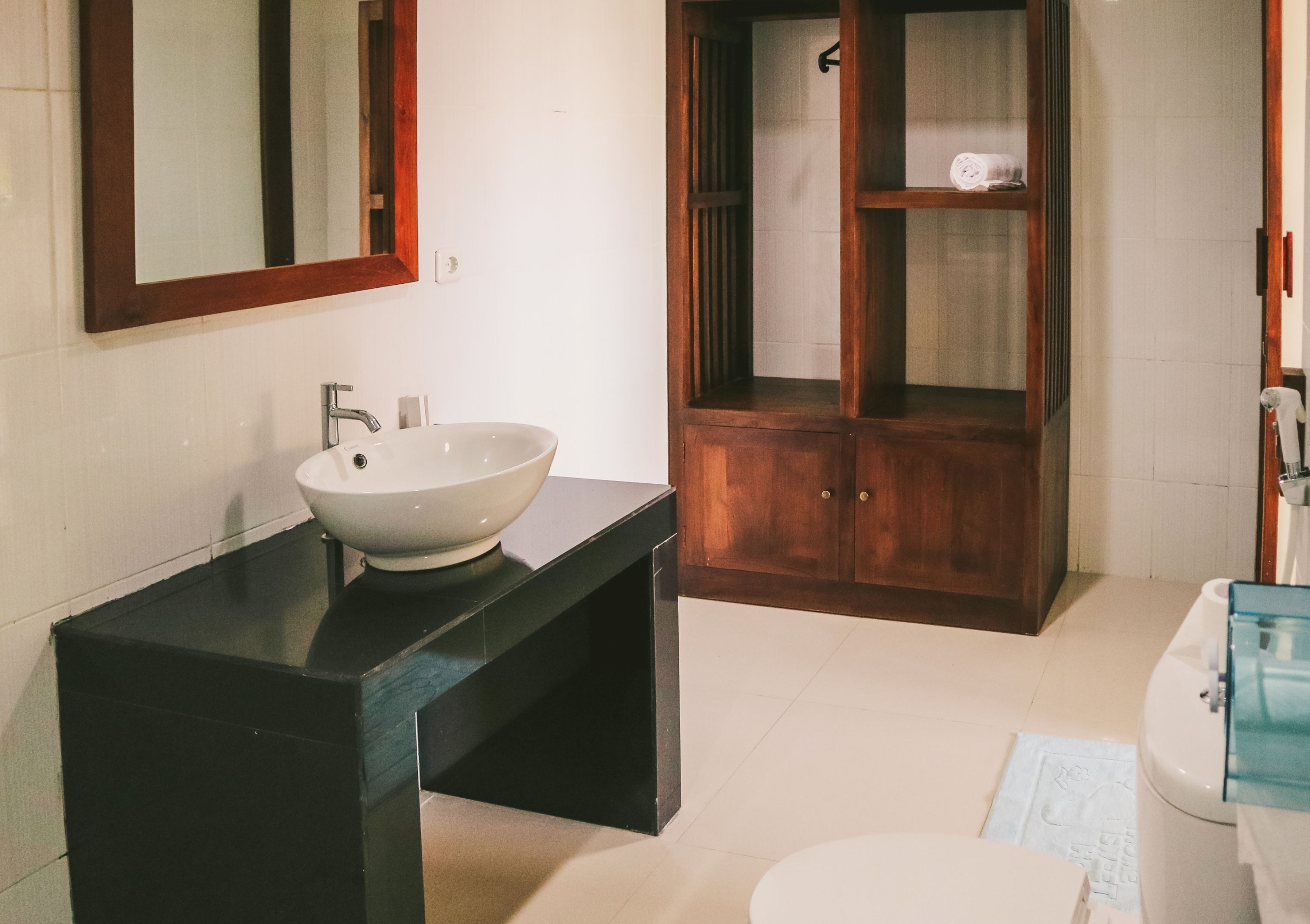 Un baño con lavabo blanco, encimera oscura, mueble de madera y váter blanco.