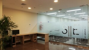 Un espacio de oficina moderno con divisiones de vidrio, un escritorio de madera y una planta en maceta.