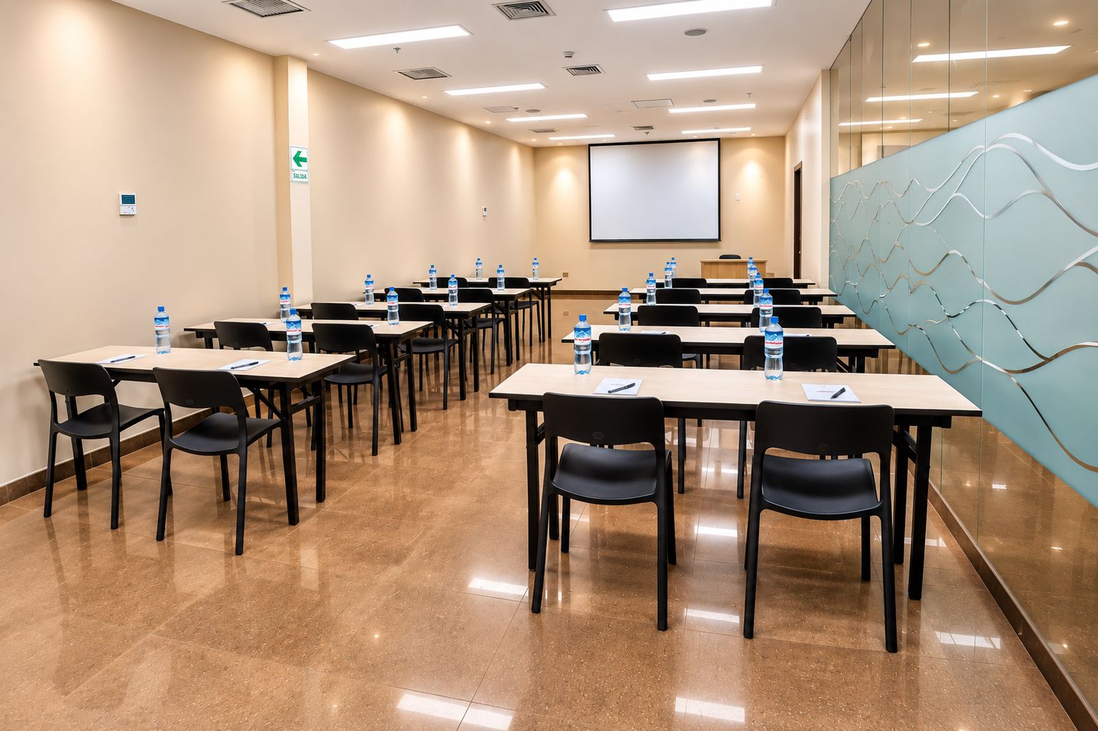 A conference room with tables, chairs, water bottles, a projector screen, and a wall with a wavy design.