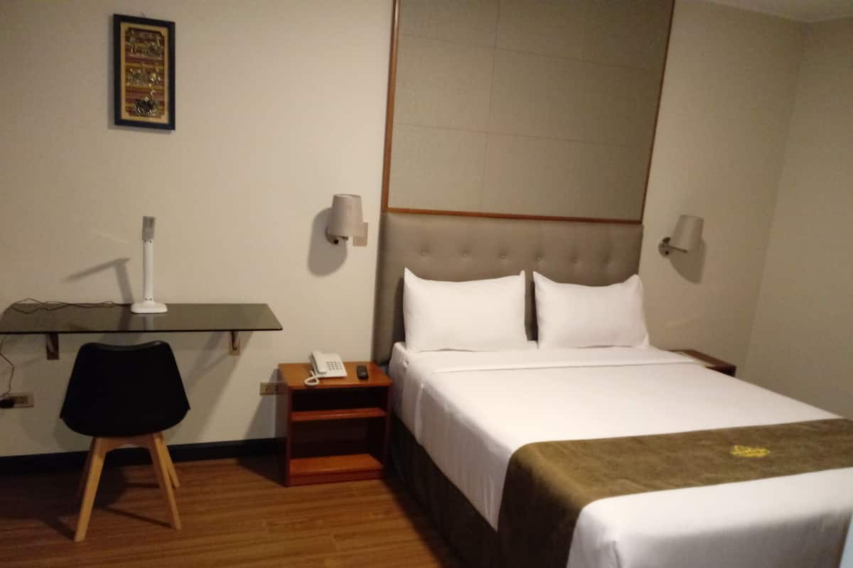 A hotel room with a bed, bedside table, lamp, and a chair.