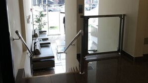 Un moderno vestíbulo de hotel con una escalera de cristal, un mostrador de recepción y vistas a la calle.